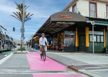 Man riding bike in cycle lane past shops