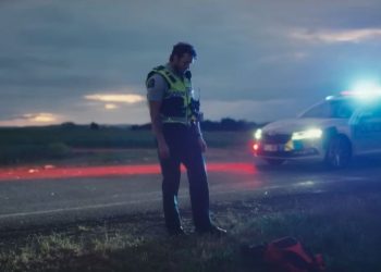 New Zealand police officer actor standing in front of patrol car