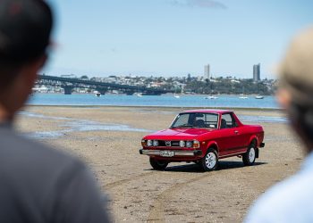 Subaru Brumby 1981 in red, parked on a beach, being admired