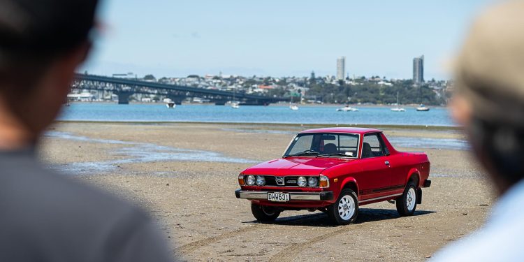 Subaru Brumby 1981 in red, parked on a beach, being admired