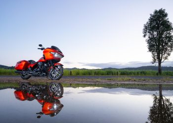 Harley Davidson Road Glide in orange, parked with a reflection below