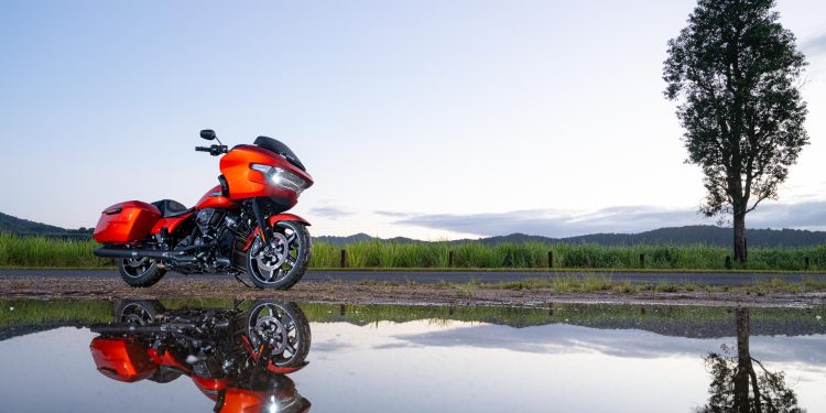 Harley Davidson Road Glide in orange, parked with a reflection below