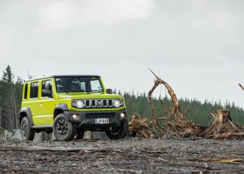 Suzuki Jimny 5-door in green, parked on a forestry ground with trees around