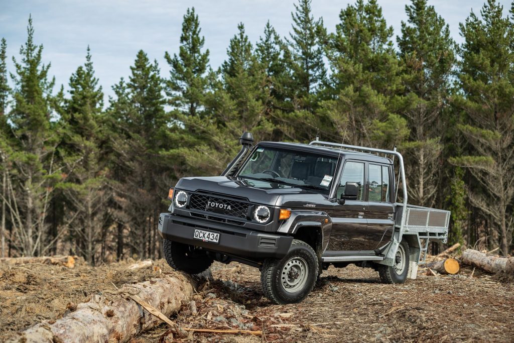 2024 Toyota Land Cruiser 70 LT Double Cab flexing on top of a log in a forest