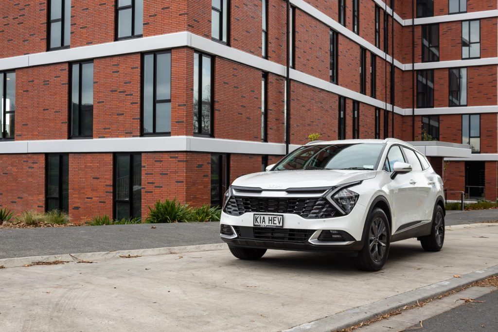 Kia Sportage Earth Hybrid, with a large brick building behind it