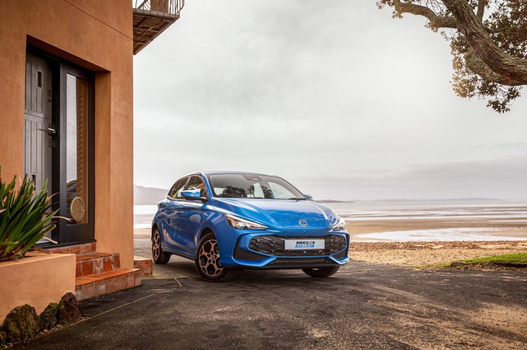 MG3 Hybrid+ Essence in blue, parked in front of Rangitoto island