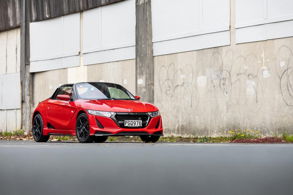 Honda S660 in red, parked next to a rustic wall