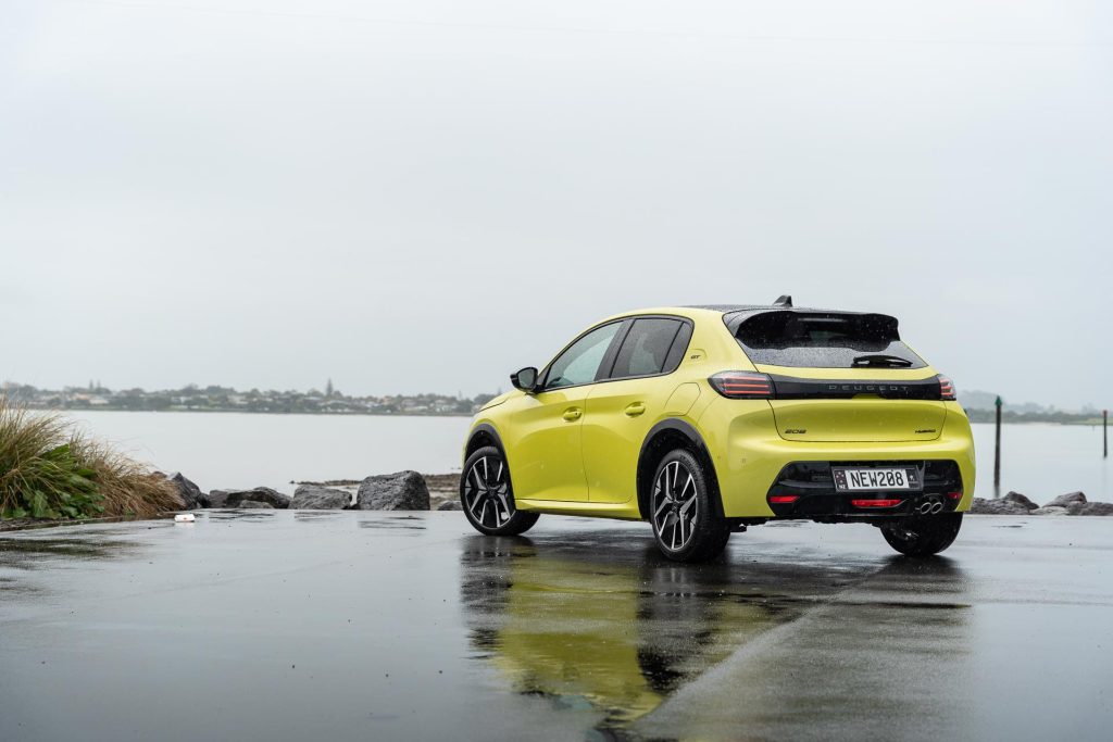 Peugeot 208 GT Hybrid in yellowish green, parked in the rain next to a water view