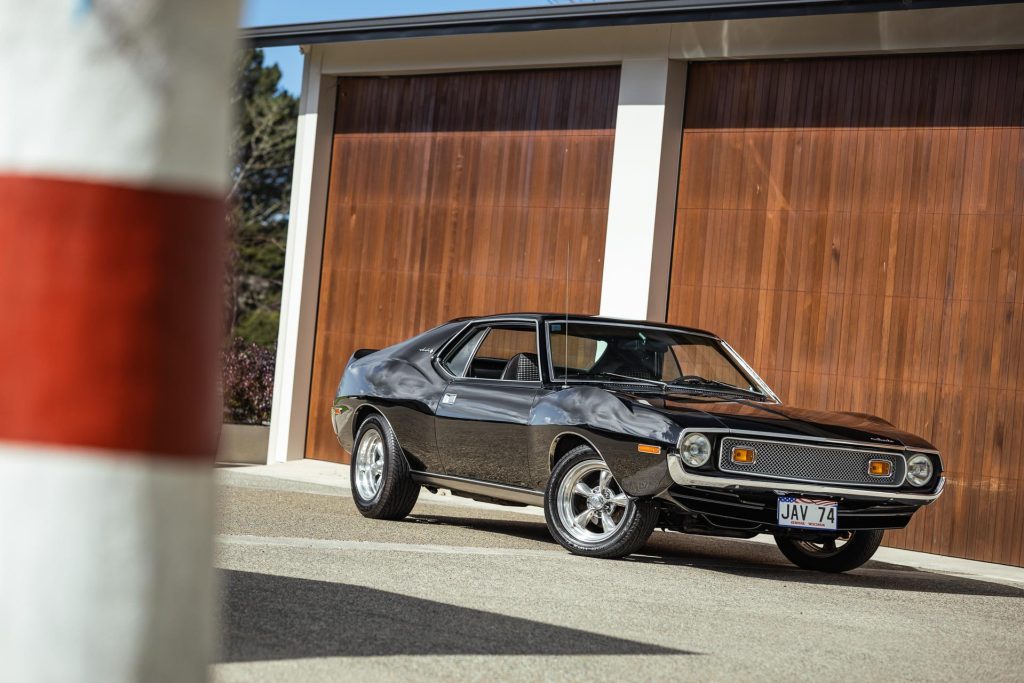 1974 AMC Javelin 401 in black, parked in front of a large garage