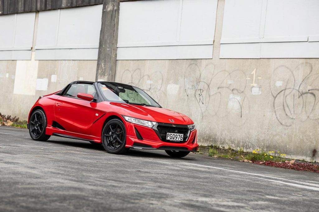 Front quarter shot of the Honda S660 Mugen RA, in red next to a graffiti'd wall