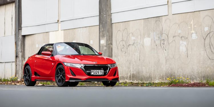 Honda S660 Mugen in red, parked in front of an urban wall