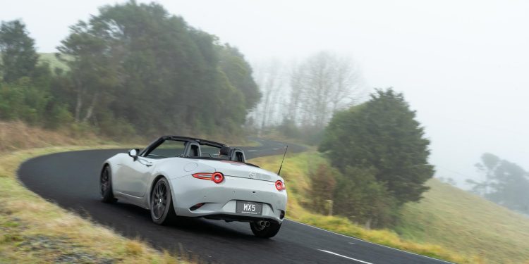 Mazda MX-5 cornering at pace, shown from the rear, on a foggy road