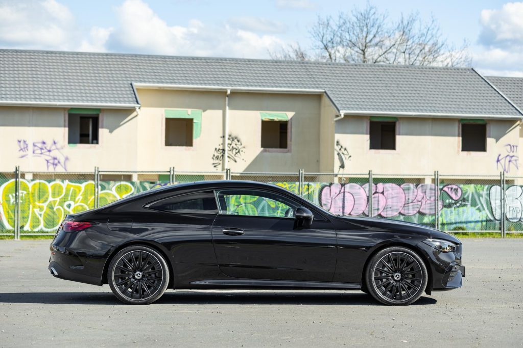 2024 Mercedes-Benz CLE 300 side profile, in front of graffiti covered wall and houses