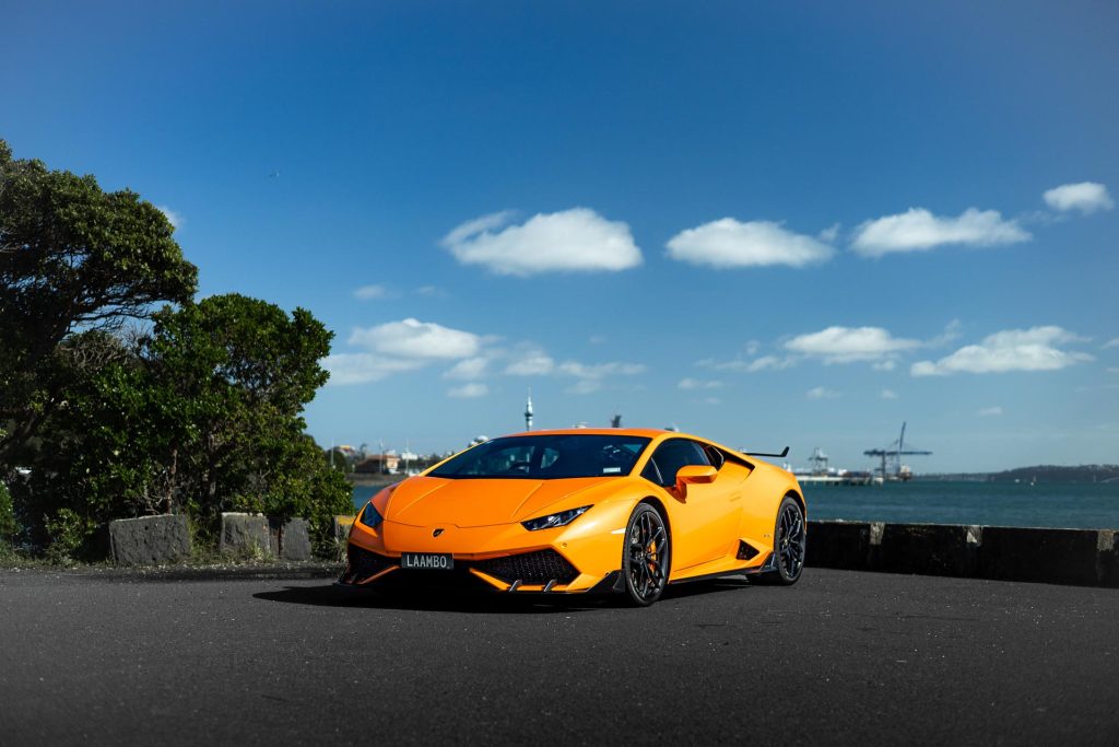 Lamborghini Huracan in orange, parked in front of Auckland's harbour