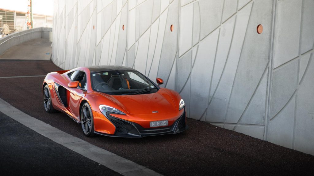 McLaren 650S in orange, parked next to white wall