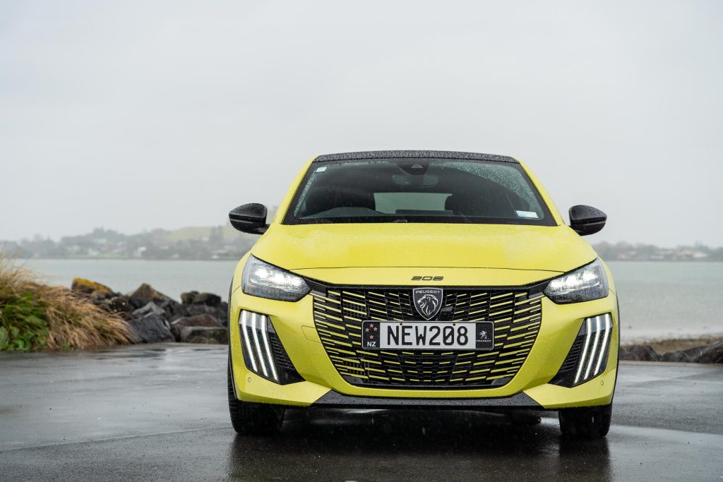 Front profile of the 2024 Peugeot 208 GT Hybrid, parked near the water on a gloomy day