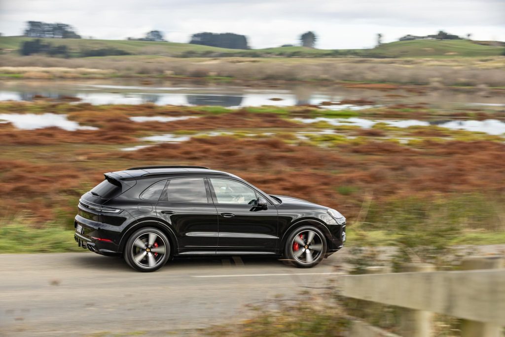 Side panning profile, with bog behind the road, showing the 2024 Porsche Cayenne