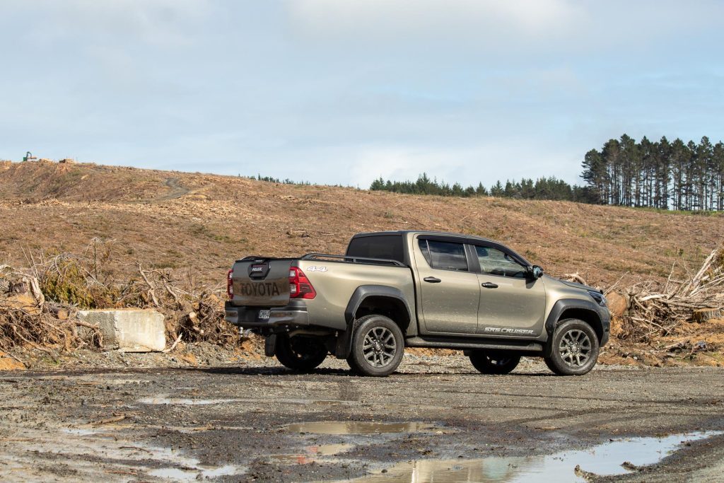 2024 Toyota Hilux SR5 Cruiser Hybrid rear side profile shot, parked on gravel and mud