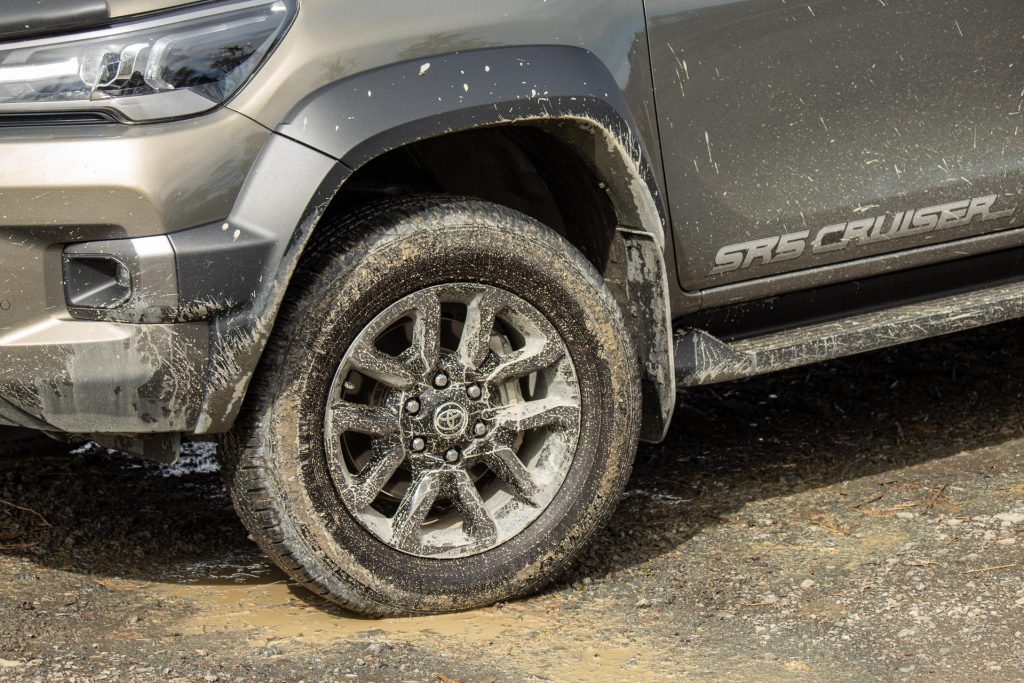 Front wheel detail of the 2024 Toyota Hilux SR5 Cruiser Hybrid, caked in mud