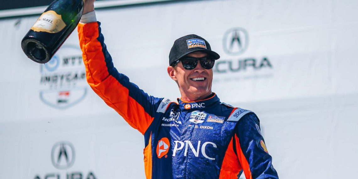 Scott Dixon holding up a bottle of Champagne and smiling