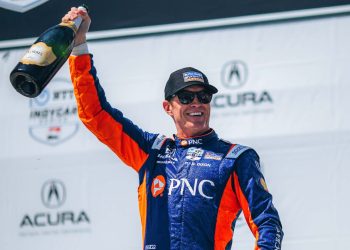 Scott Dixon holding up a bottle of Champagne and smiling