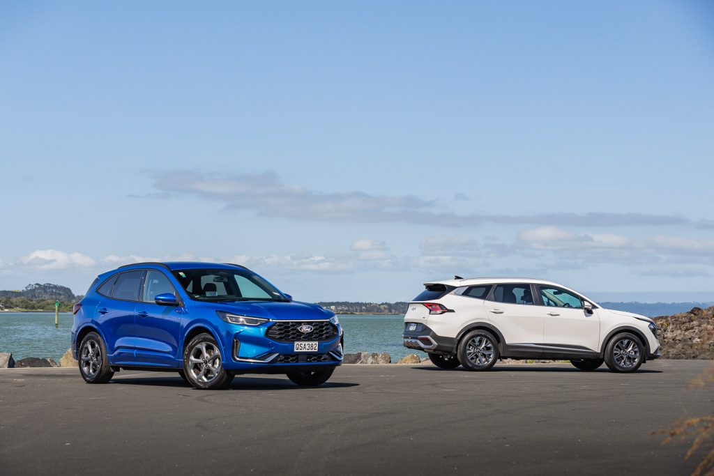 Blue Ford Escape ST-Line X FHEV AWD parked near Kia Sportage HEV Earth in white