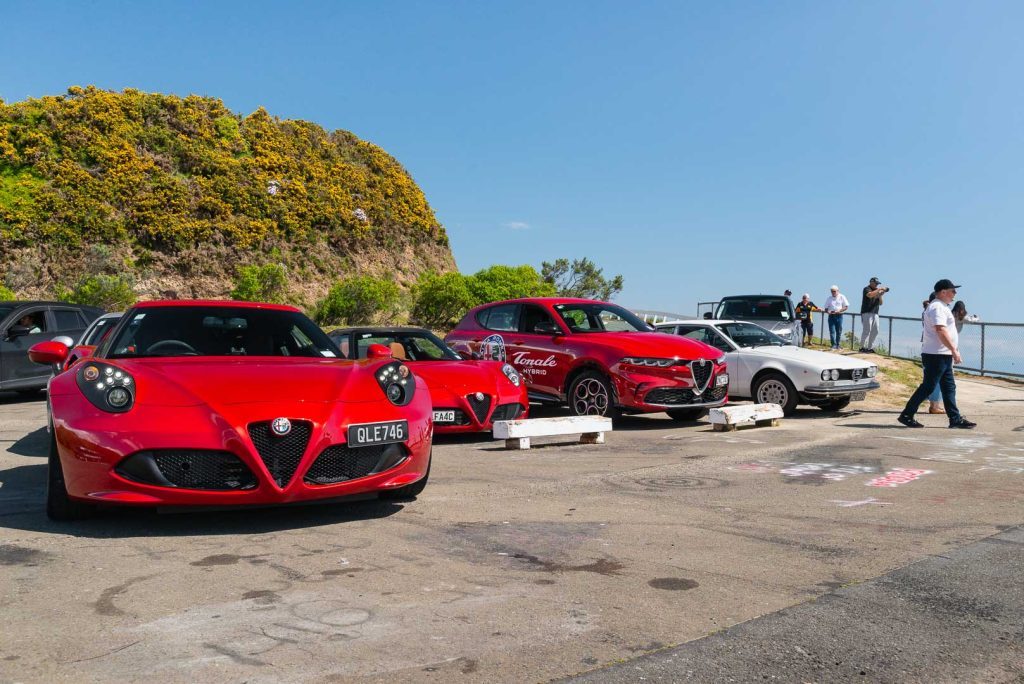 Lineup of Alfa Romeo 4C, Tonale, and Alfasud, parked in picturesque location