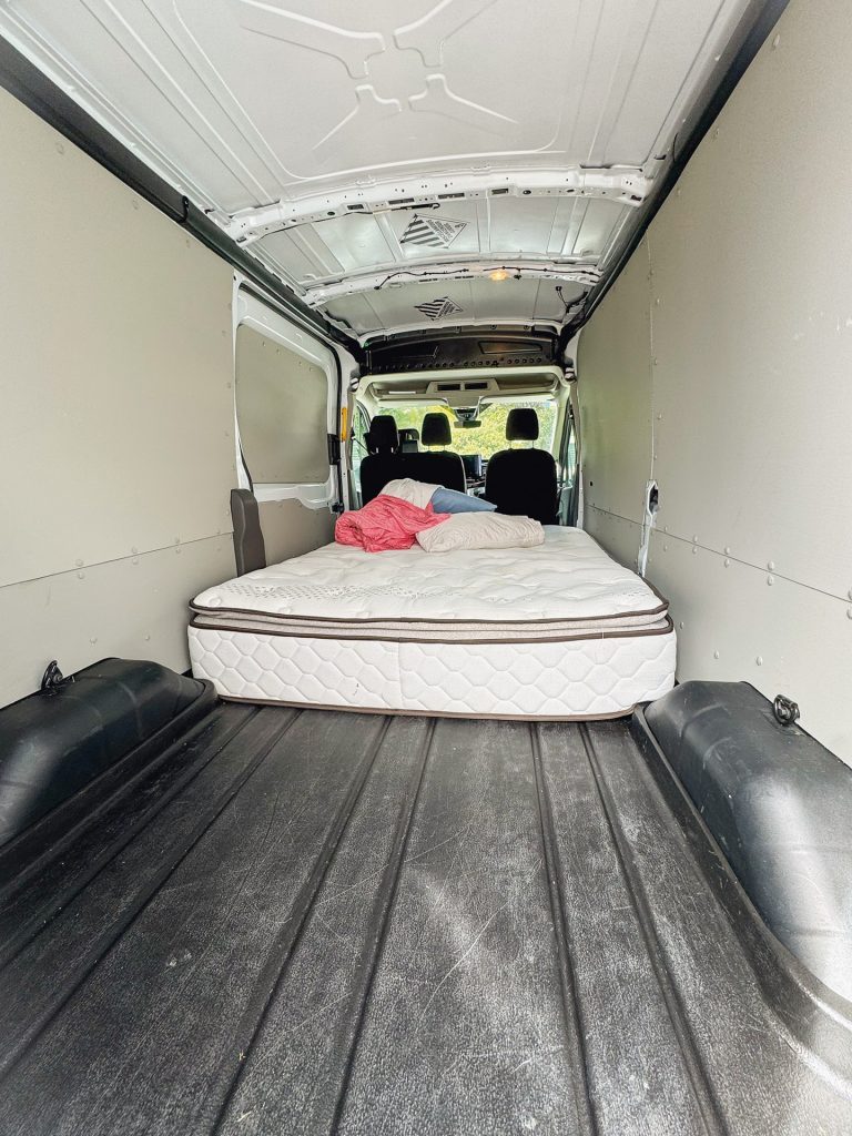 Van interior with a mattress, red blanket, and pillow, showing a converted living space for travel or camping