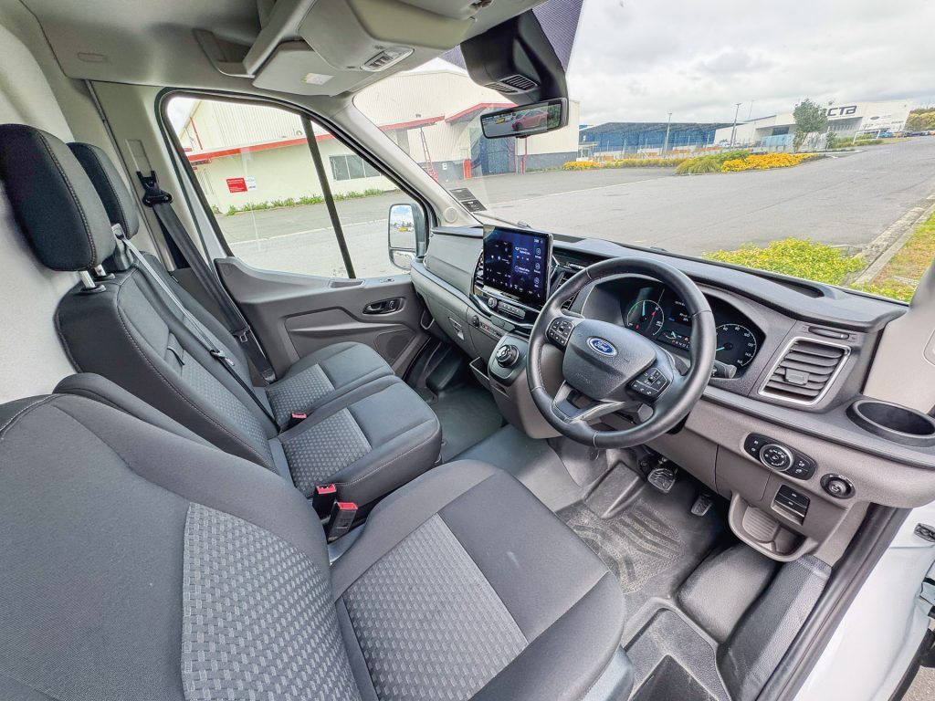 The interior of a Ford vehicle's driver's cabin with black seats, a dashboard touchscreen display, and a steering wheel with control buttons