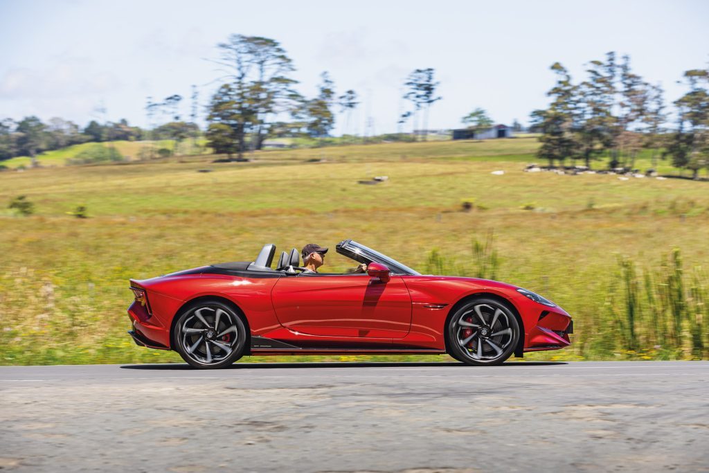 Red MG Cyberster convertible, featuring scissor doors and dual-motor system, driven by a man on a scenic road