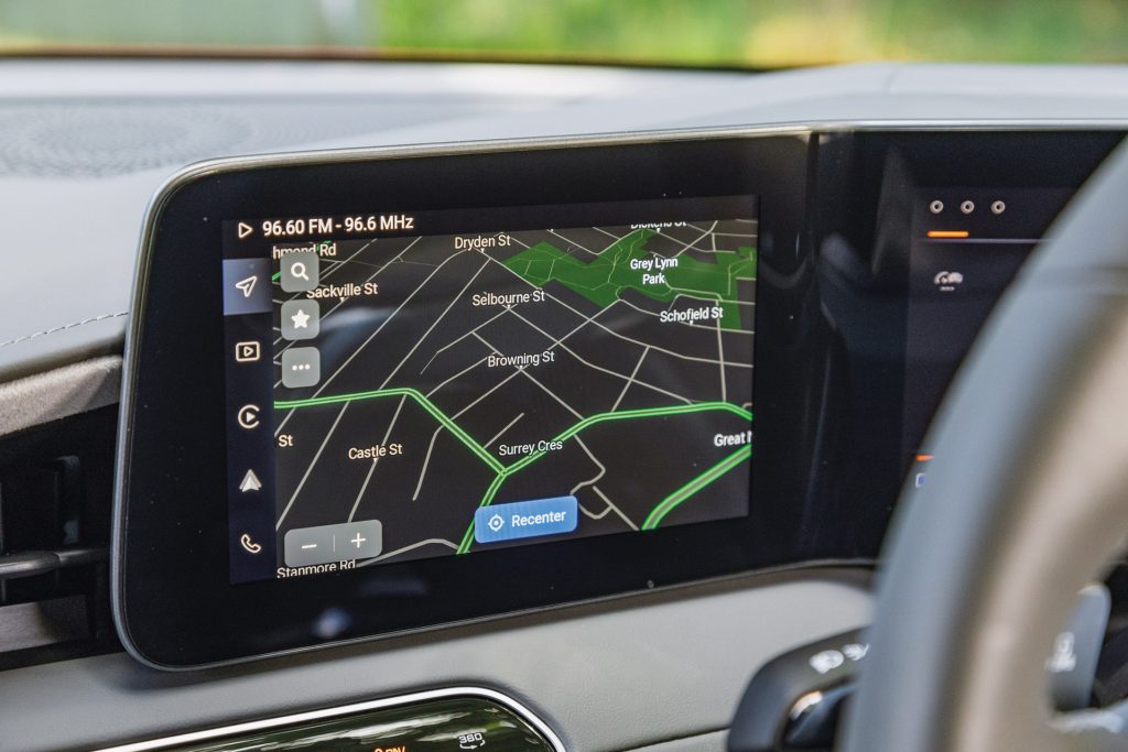 Navigation screen of a car's infotainment system showing a map with street names and a park, with icons on the side and the radio frequency displayed at the top