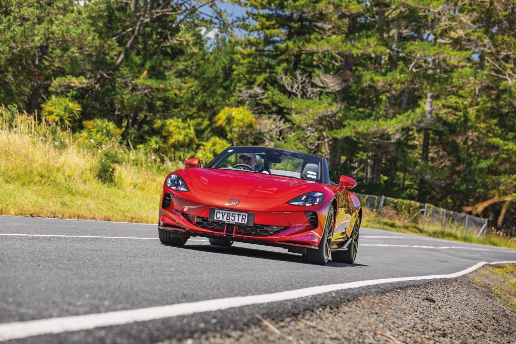 A red MG Cyberster convertible driving on a scenic road