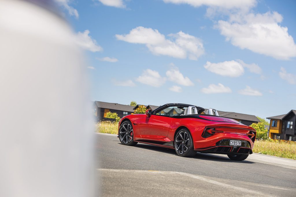 Red MG Cyberster convertible with a modern, sleek design, parked on a suburban road under a clear blue sky