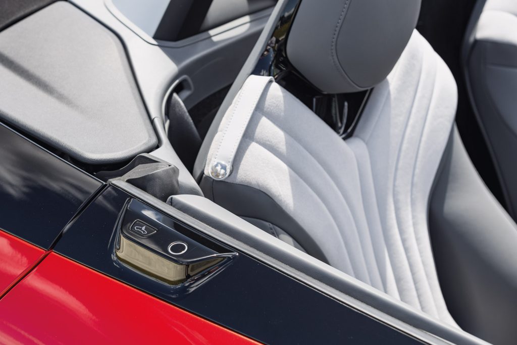 "Convertible car interior showcasing a light grey fabric passenger seat with a modern, contoured design. The control panel on the side door features two buttons for seat adjustments. The car door has a glossy black and red finish