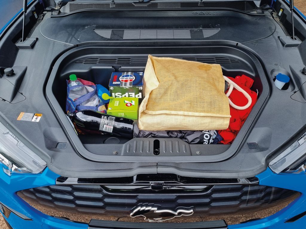 Open trunk of a blue Ford Mustang Mach-E electric SUV filled with various items for a beach outing, showcasing its practical storage capacity