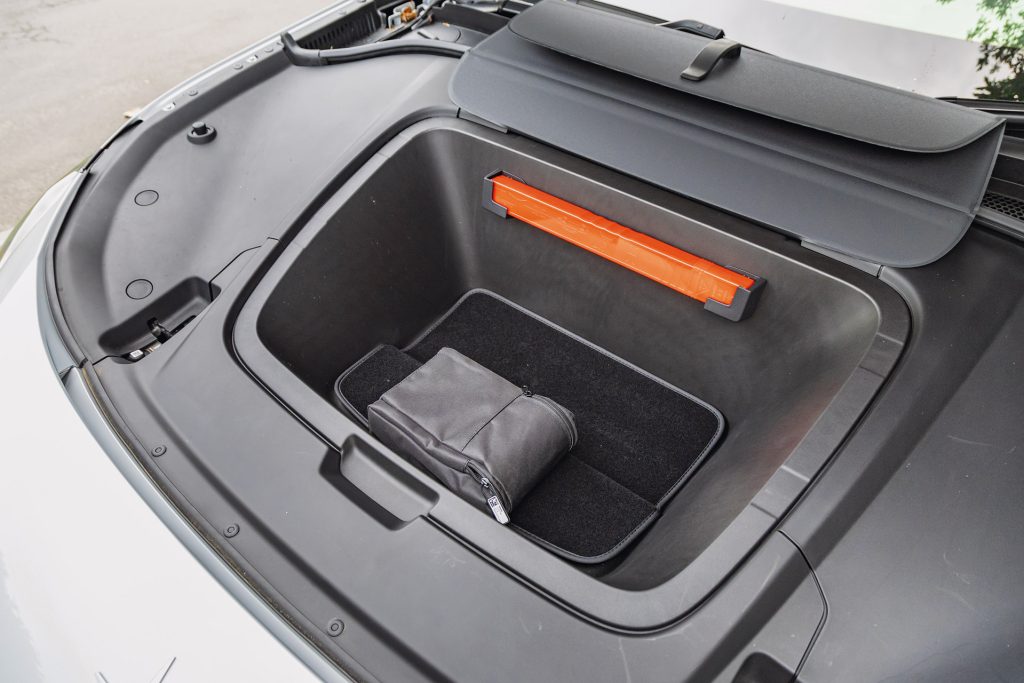 Open front trunk of the Polestar 3, showing a storage compartment with a black zippered pouch and an orange safety triangle