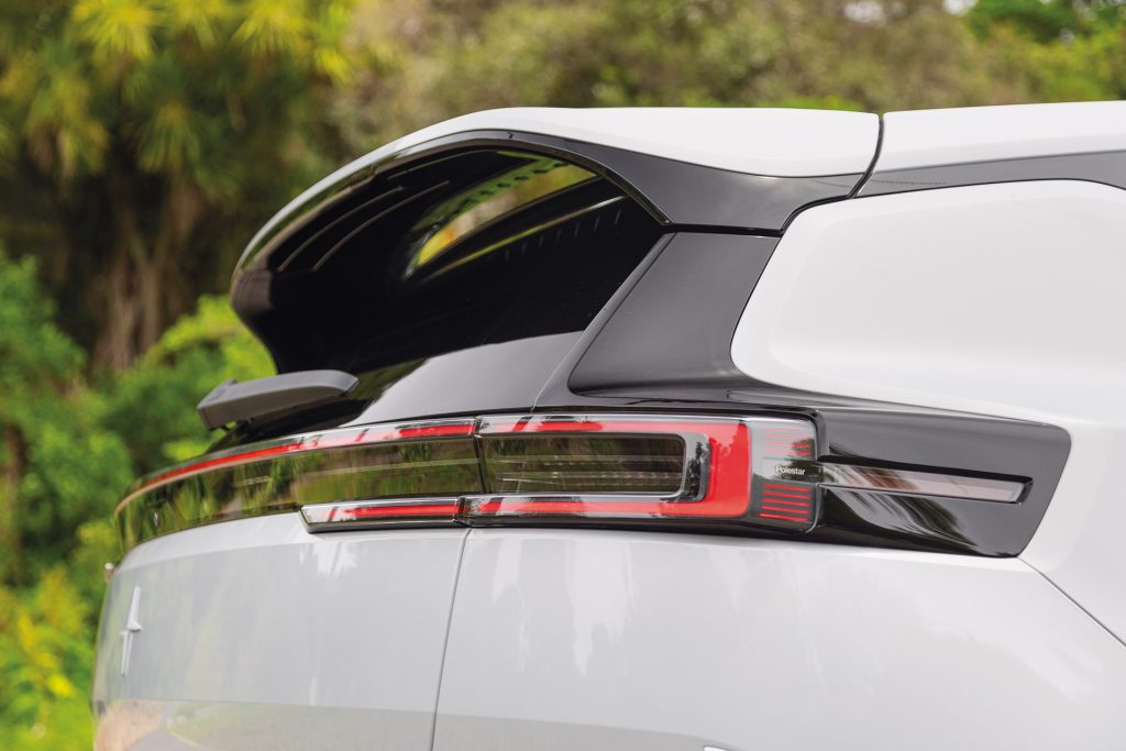 Rear section of a white Polestar car, showcasing sleek tail lights, rear spoiler, and Polestar logo with outdoor greenery in the background