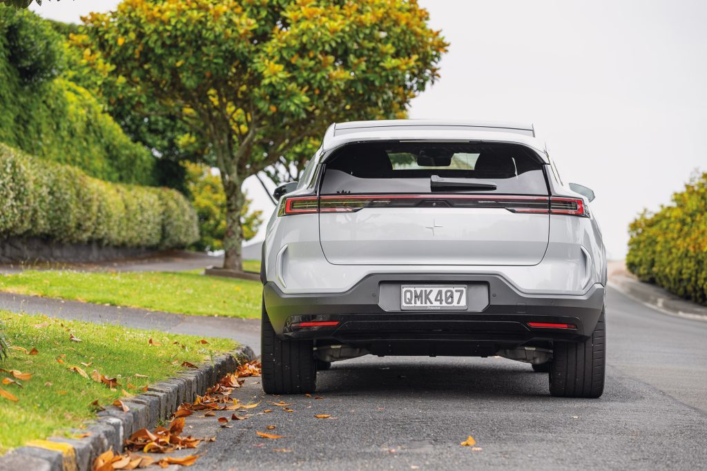 Rear view of a white Polestar 3 electric vehicle parked on a suburban road with fallen leaves and lush green trees in the background