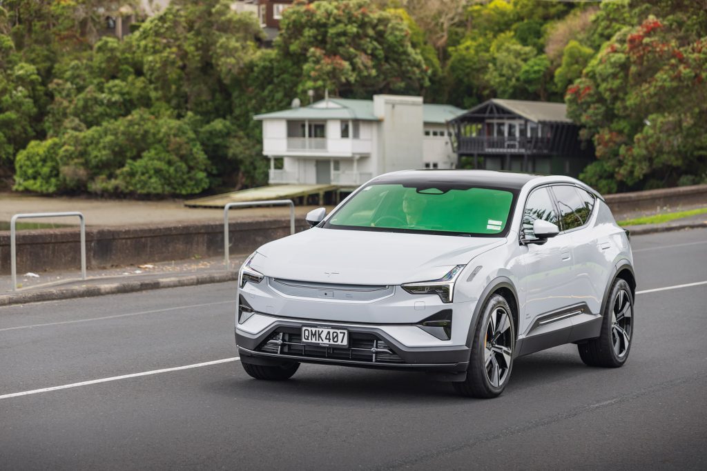 A white Polestar 3 electric SUV driving on a suburban road, highlighting its modern design and LED headlights