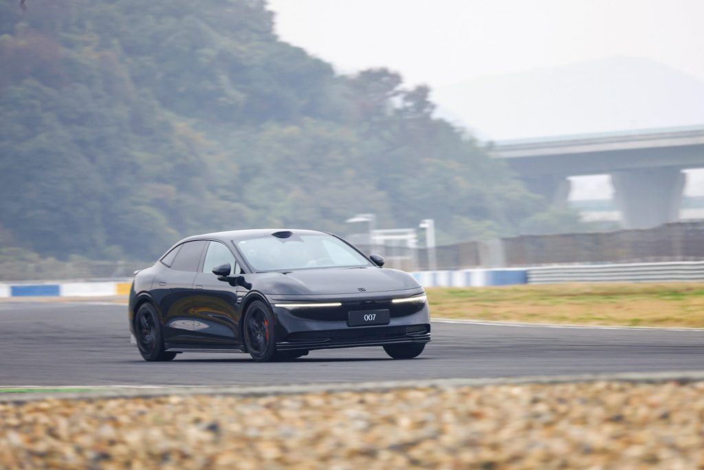 Sleek black Zeekr driving on a racetrack with lush green hills and bridge in the background